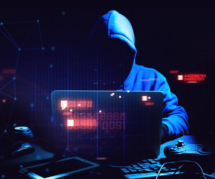 Chroń swoje dane i urządzenia podczas pracy zdalnej - postaw na cyberbezpieczeństwo. Grafika prezentuje postać hakera siedzącego przed laptopem. Haker założoną ma bluzę z kapturem, nie widać mu twarzy.